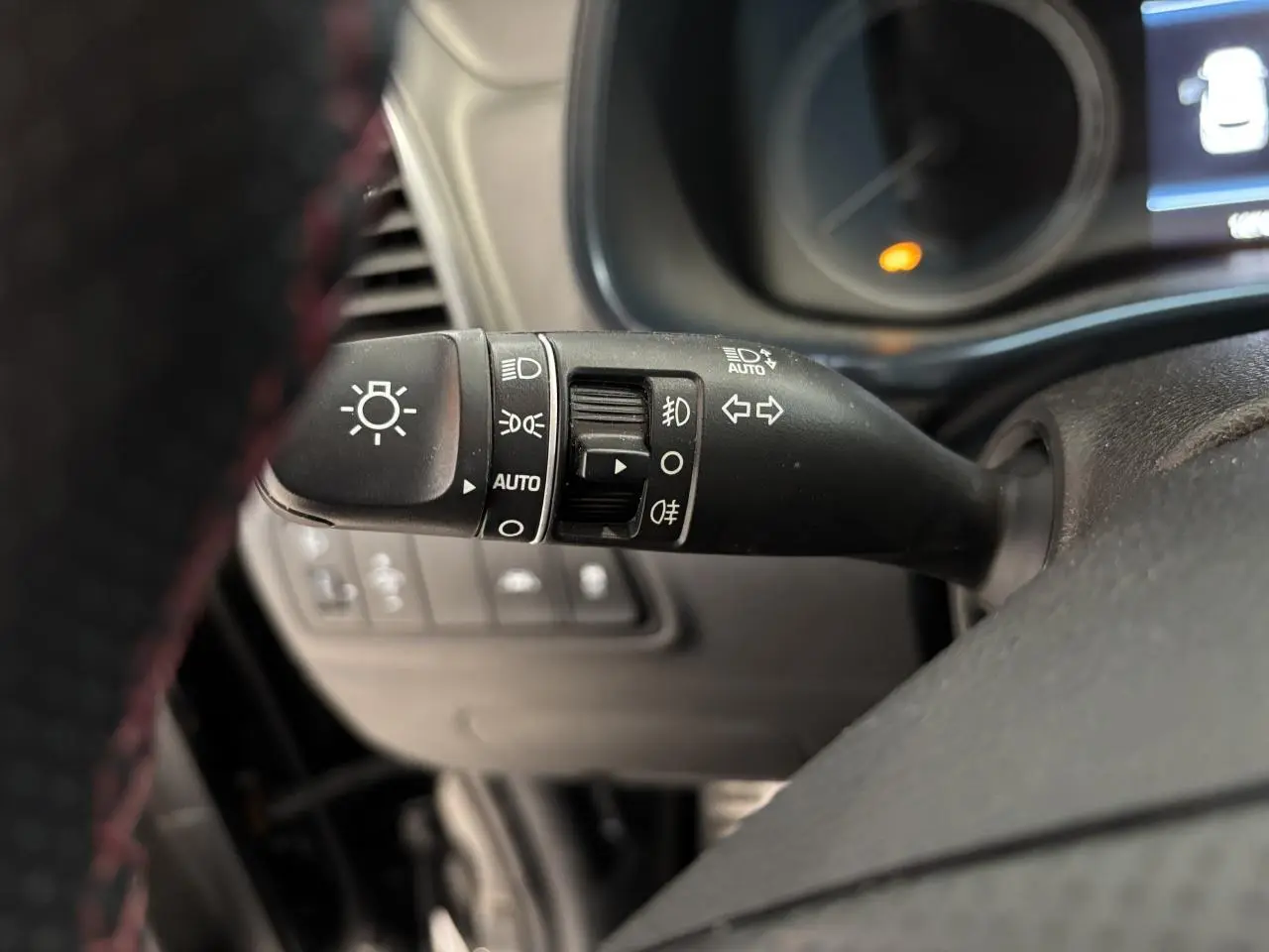 Gros plan sur la manette de commande des feux et clignotants du Hyundai Tucson noir, intérieur avec volant perforé.