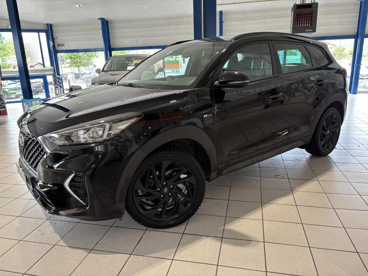 Hyundai Tucson noir en 3/4 avant droit, avec jantes alliage noires et badge N Line visible sur l'aile avant.