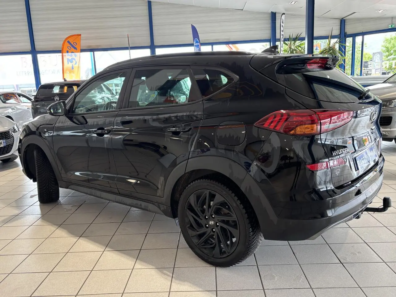 Vue 3/4 arrière gauche du Hyundai Tucson noir métallisé avec jantes alliage noires et attelage en concession.