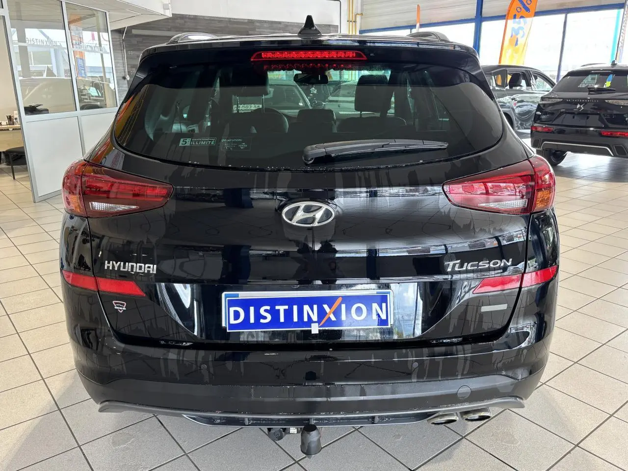 Vue arrière d'un Hyundai Tucson noir métallisé avec double sortie d'échappement et logo distinctif en concession.