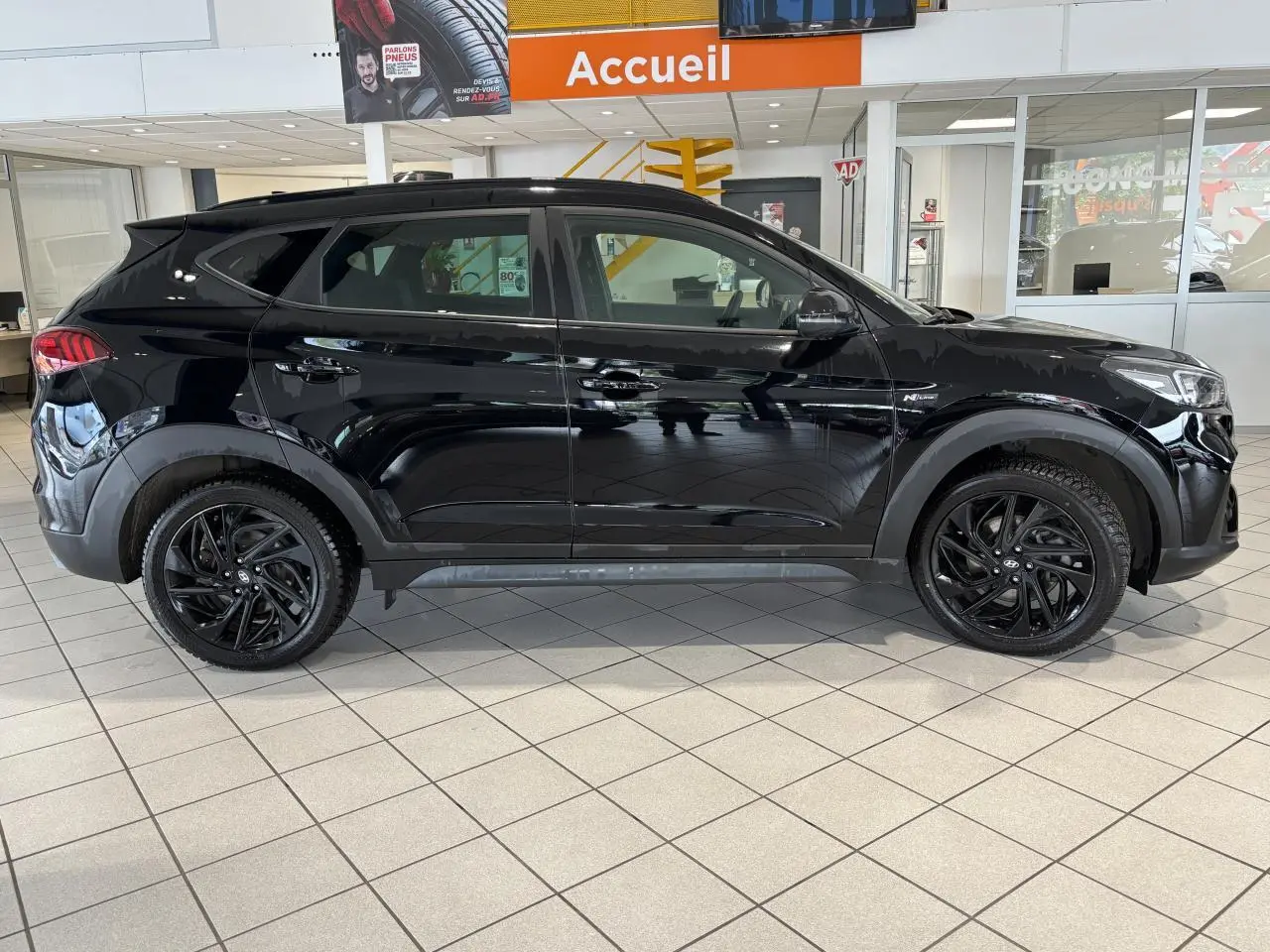 Vue latérale droite d'un Hyundai Tucson noir métallisé N Line avec jantes alliage noires en showroom.