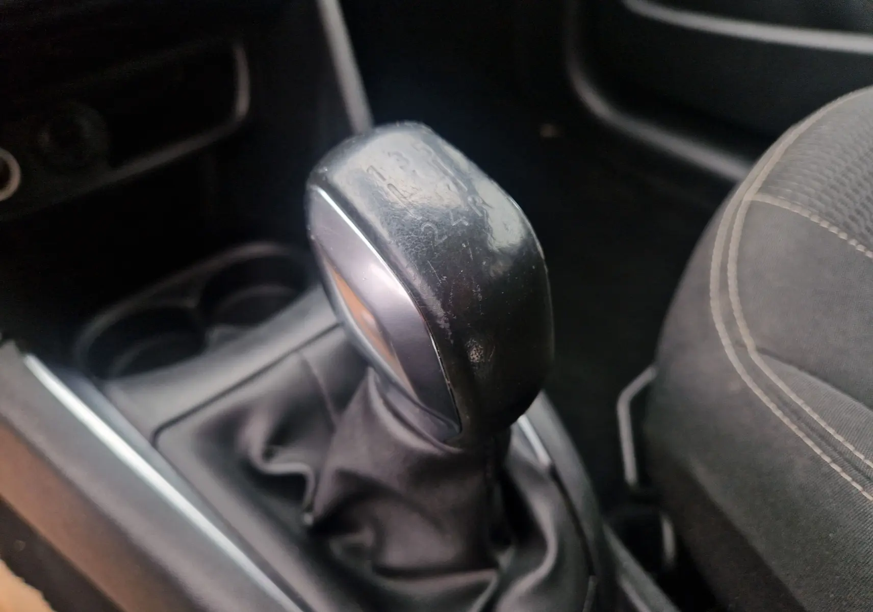 Gros plan sur le levier de vitesses manuel noir de la Peugeot 208 blanc nacré, avec siège tissu gris à droite.