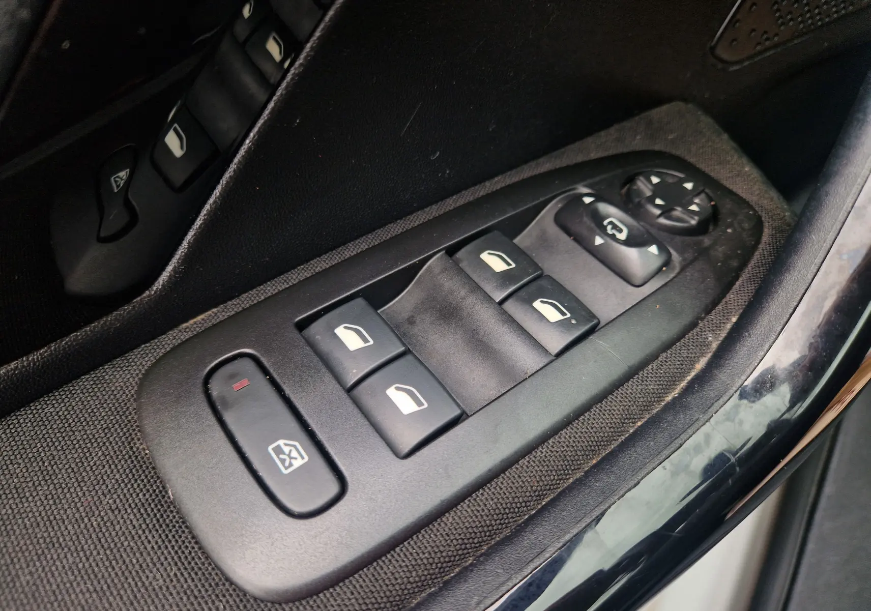 Gros plan sur les commandes de lève-vitres et réglage des rétroviseurs côté conducteur d’une Peugeot 208 blanche nacrée.