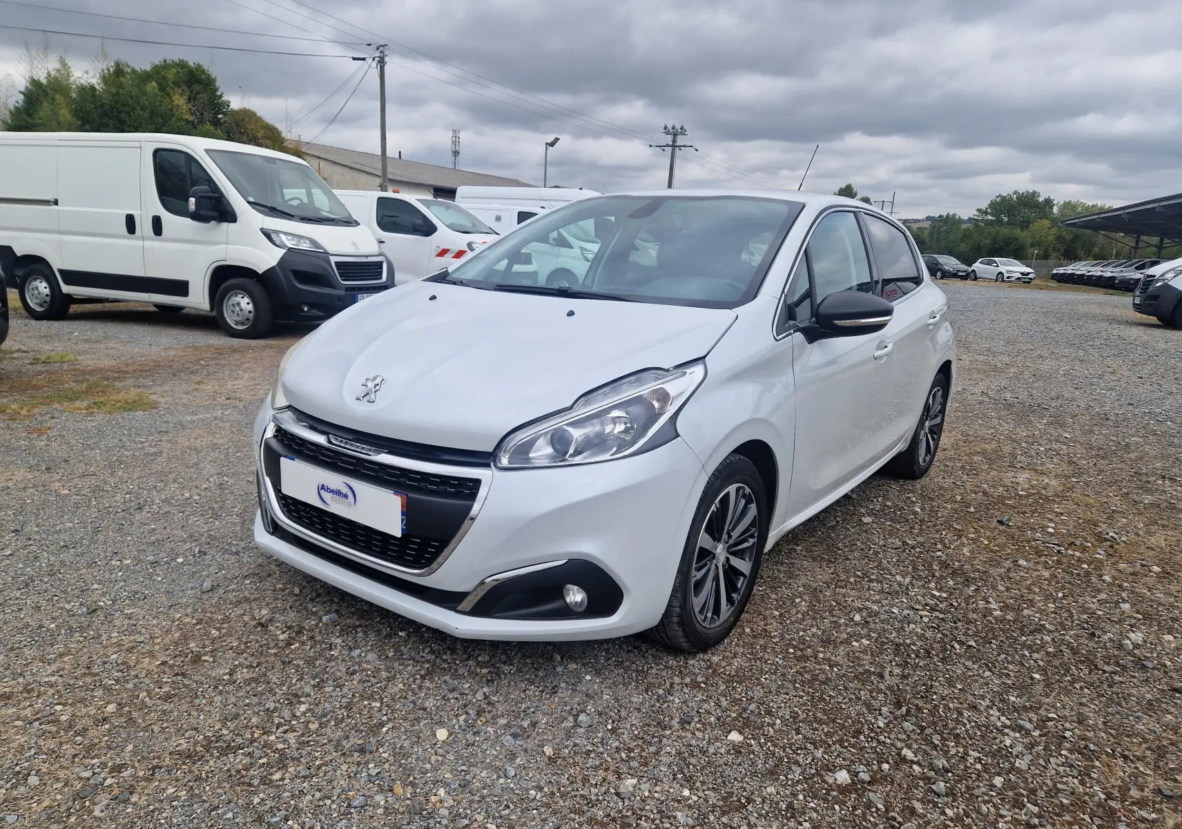 Peugeot 208 blanc nacré vue 3/4 avant droit, avec jantes alliage bi-ton et calandre noire distinctive.