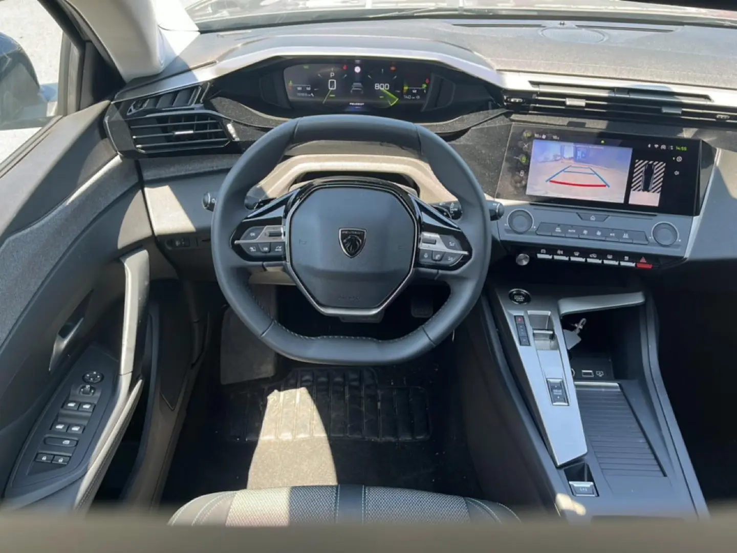 Vue intérieure frontale du poste de conduite de la Peugeot 308 gris, avec volant multifonction et écran tactile affichant la caméra de recul.