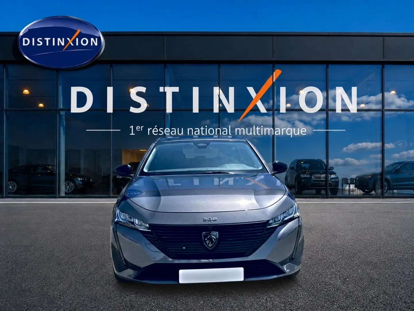 Peugeot 308 gris vue de face, avec calandre noire et logo lion distinctif, devant une vitrine Distinxion.
