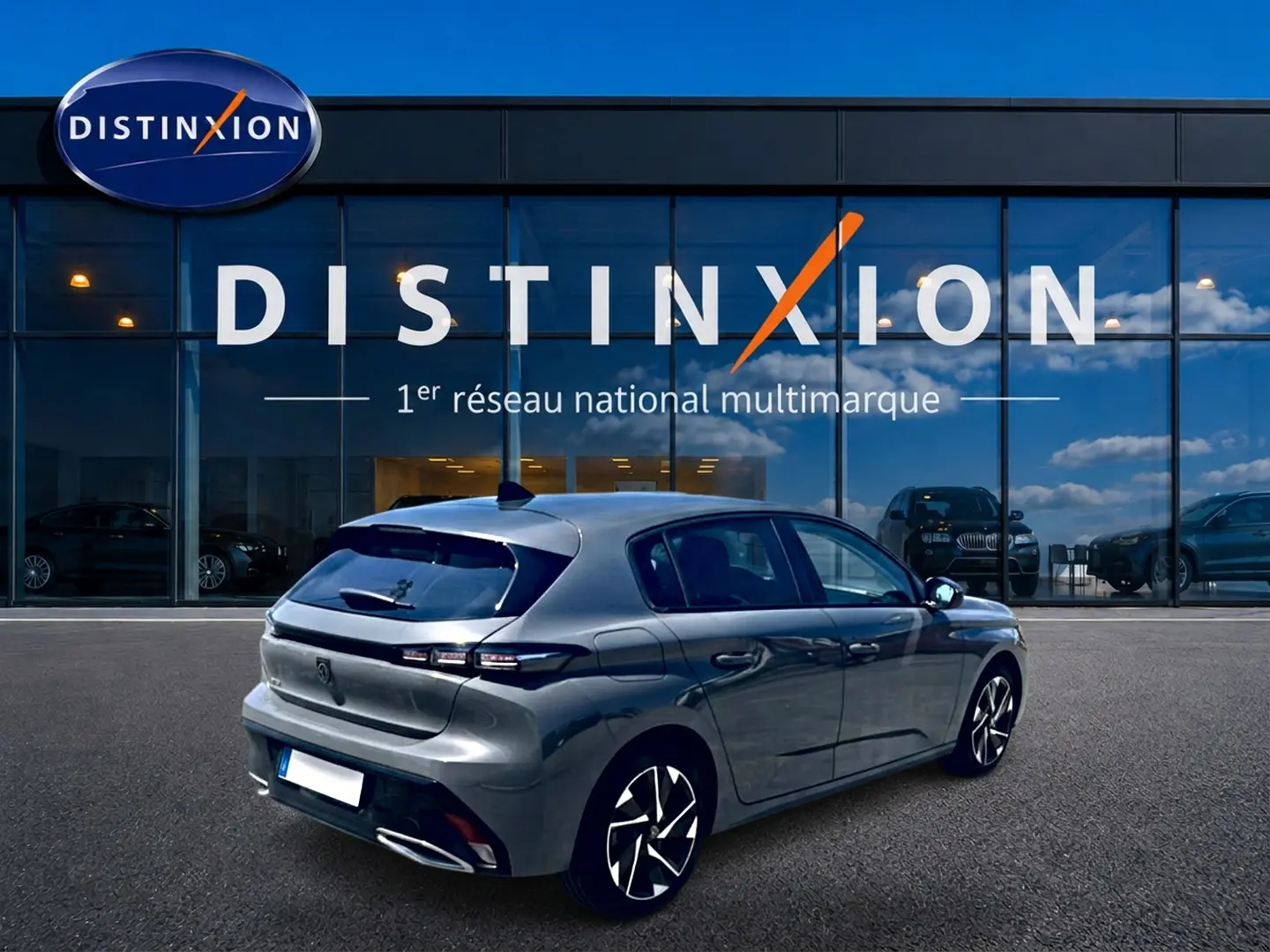 Vue 3/4 arrière droite d'une Peugeot 308 gris métallisé garée devant une vitrine avec logo Distinxion.
