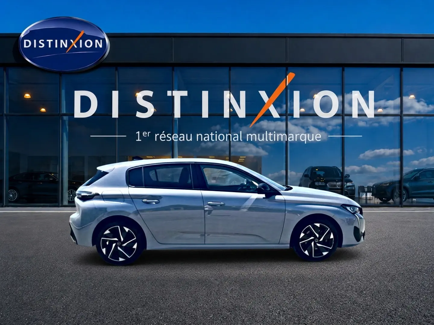 Profil droit d'une Peugeot 308 gris métallisé garée devant une vitrine avec logo Distinxion.