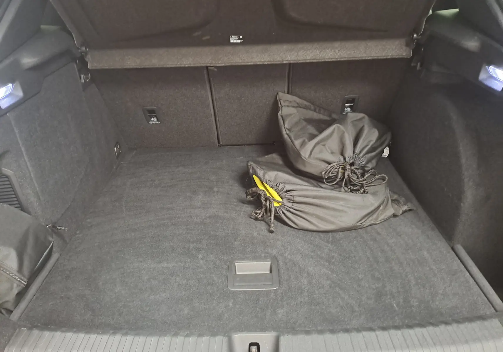 Coffre ouvert vu de l'arrière d'une CUPRA TERRAMAR 1.5 eHybrid bleu cosmos avec sacoches noires à l'intérieur.