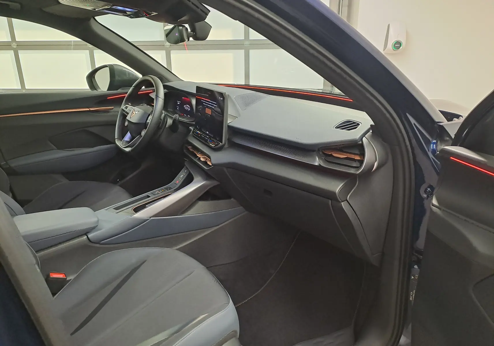 Vue intérieure côté conducteur du CUPRA TERRAMAR bleu cosmos 2025, avec tableau de bord moderne et éclairage d’ambiance rouge.