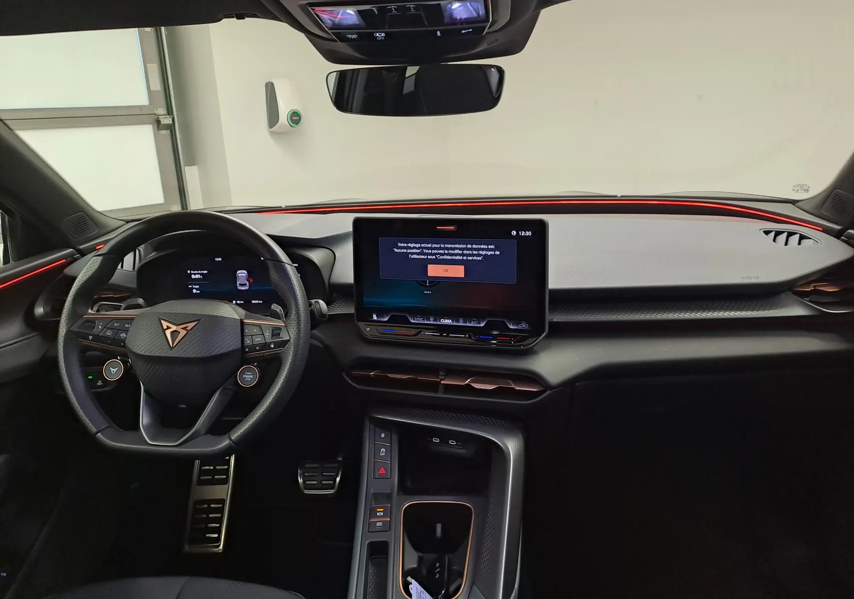 Vue intérieure avant du tableau de bord du CUPRA TERRAMAR 2025 avec éclairage d'ambiance rouge et écran tactile central.