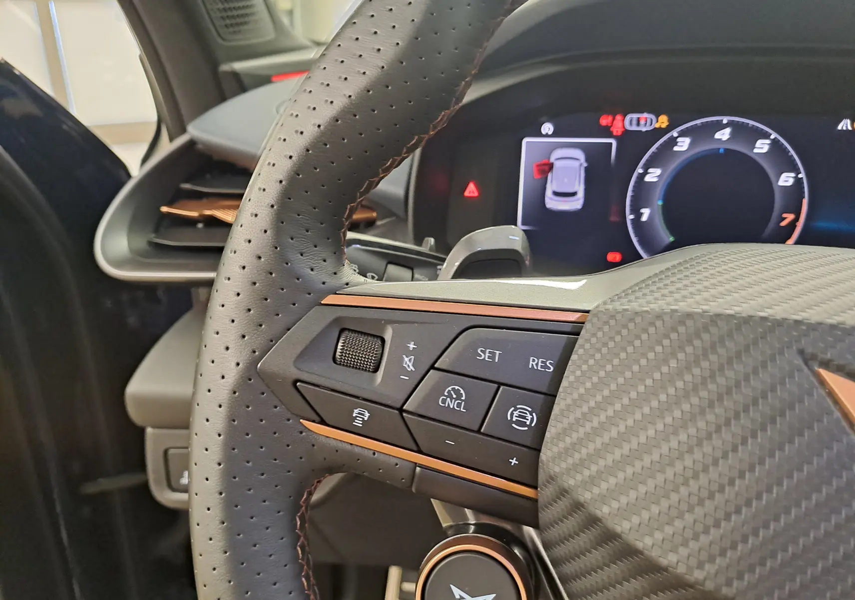 Gros plan sur le volant perforé et les commandes du CUPRA Terramar 1.5 eHybrid, avec tableau de bord numérique en arrière-plan.