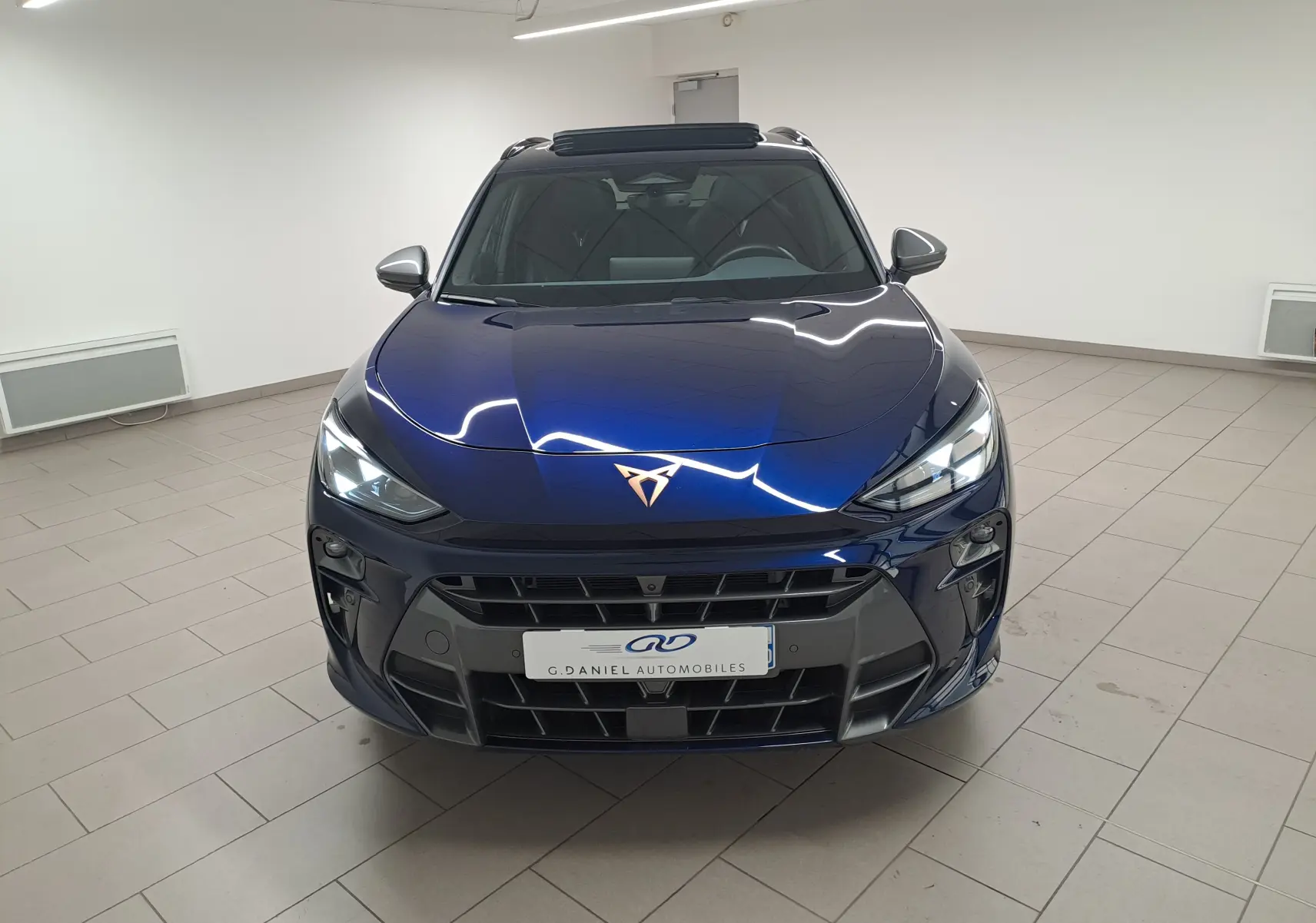 Vue avant d'une CUPRA TERRAMAR 1.5 eHybrid bleu cosmos avec toit ouvrant panoramique en intérieur showroom.