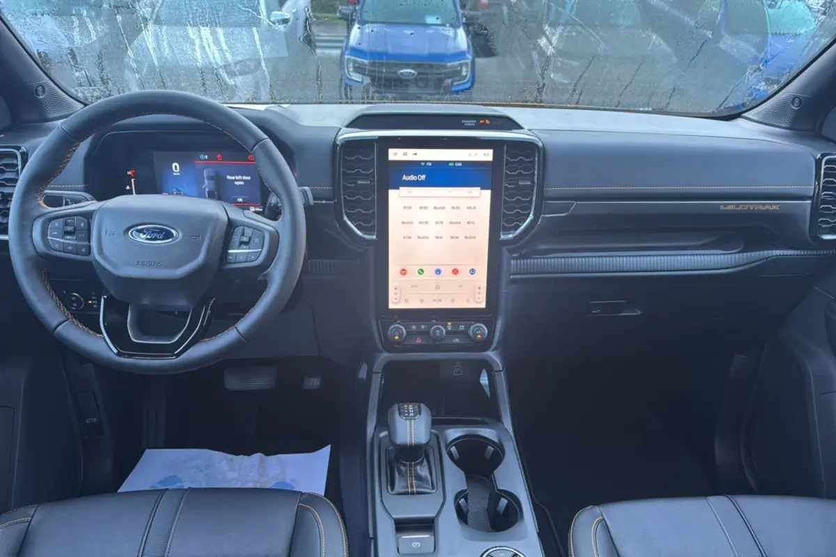 Vue intérieure avant du Ford Ranger Wildtrak 2026, tableau de bord noir avec écran tactile vertical et volant multifonctions.
