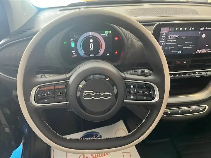 Vue rapprochée du volant de la Fiat 500 électrique gris minéral, avec tableau de bord numérique et écran tactile central.