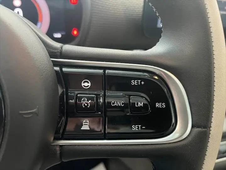 Gros plan sur les commandes de régulateur de vitesse au volant cuir noir de la FIAT 500 électrique gris minéral.