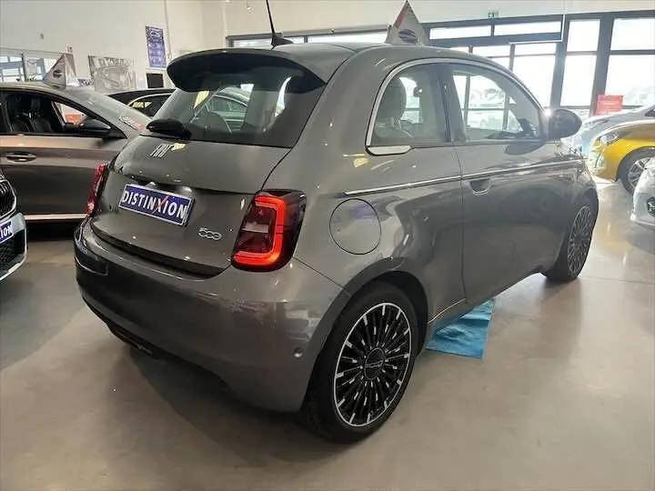 Vue 3/4 arrière droite d'une FIAT 500 électrique gris minéral métal avec feux LED et jantes noires stylisées en showroom.