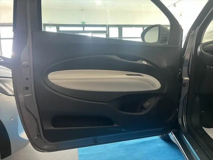 Vue intérieure de la porte côté gauche d'une Fiat 500 électrique gris minéral métal avec garniture claire.