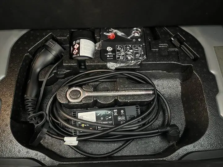 Câble de recharge électrique et outils de bord rangés dans le compartiment de la FIAT 500 électrique gris minéral.
