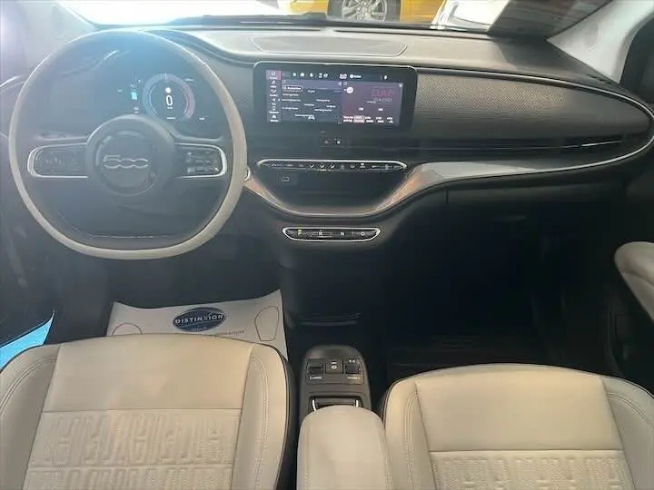 Vue intérieure avant de la Fiat 500 électrique gris minéral, avec tableau de bord numérique et sièges cuir clair.