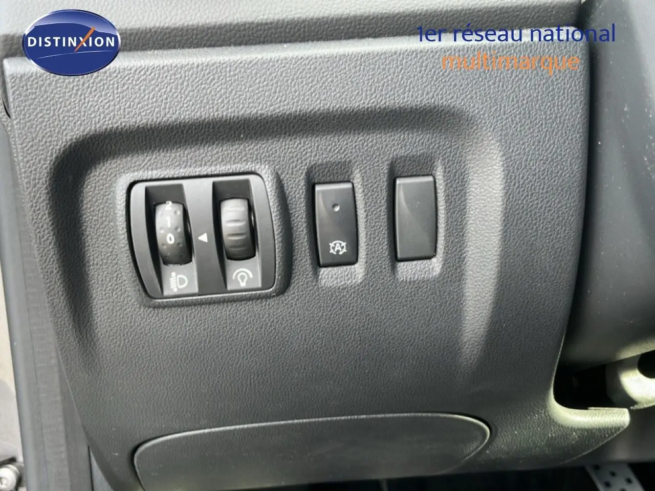 Gros plan sur les commandes de réglage des phares et du tableau de bord du Renault Captur gris, côté conducteur.