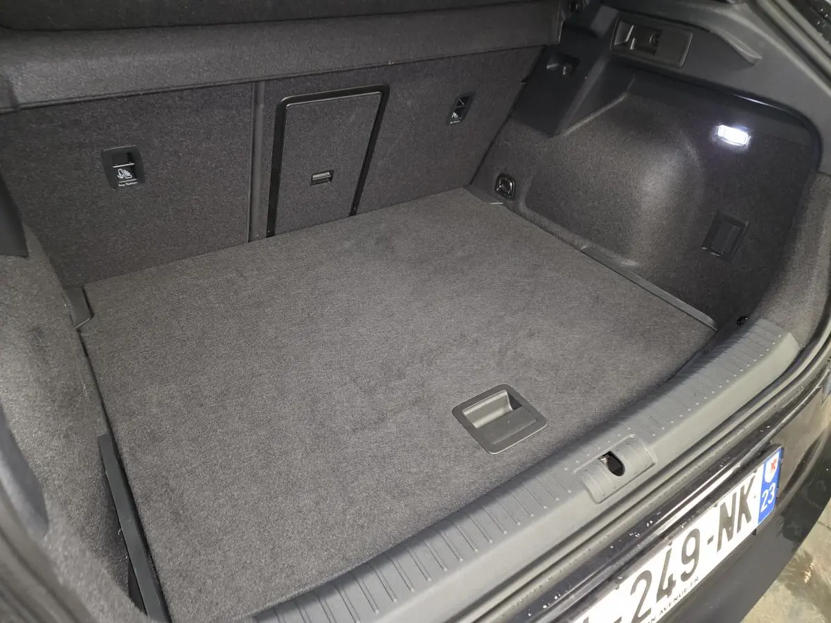 Coffre ouvert vu de l'arrière d'un CUPRA Formentor noir, avec tapis de sol gris et éclairage intérieur.