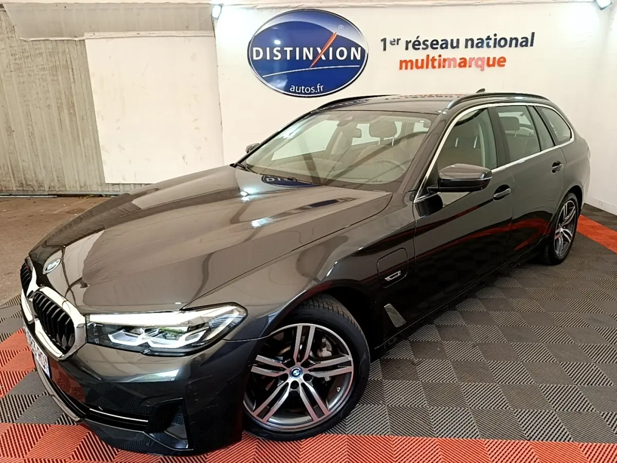BMW Série 5 Touring 530e gris clair vue 3/4 avant droit, avec jantes alliage et phares LED allumés.