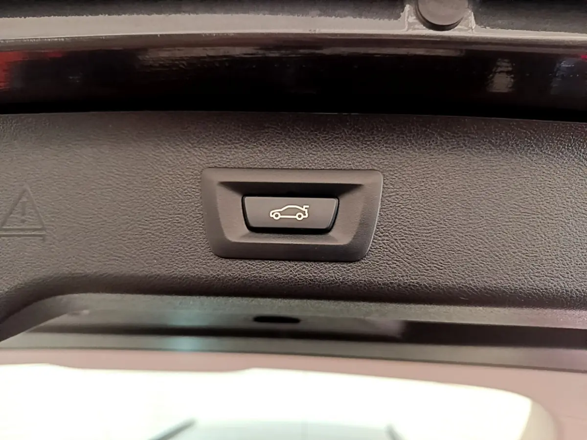 Bouton d'ouverture électrique du coffre sur la partie intérieure du hayon d'une BMW Série 5 Touring gris clair.
