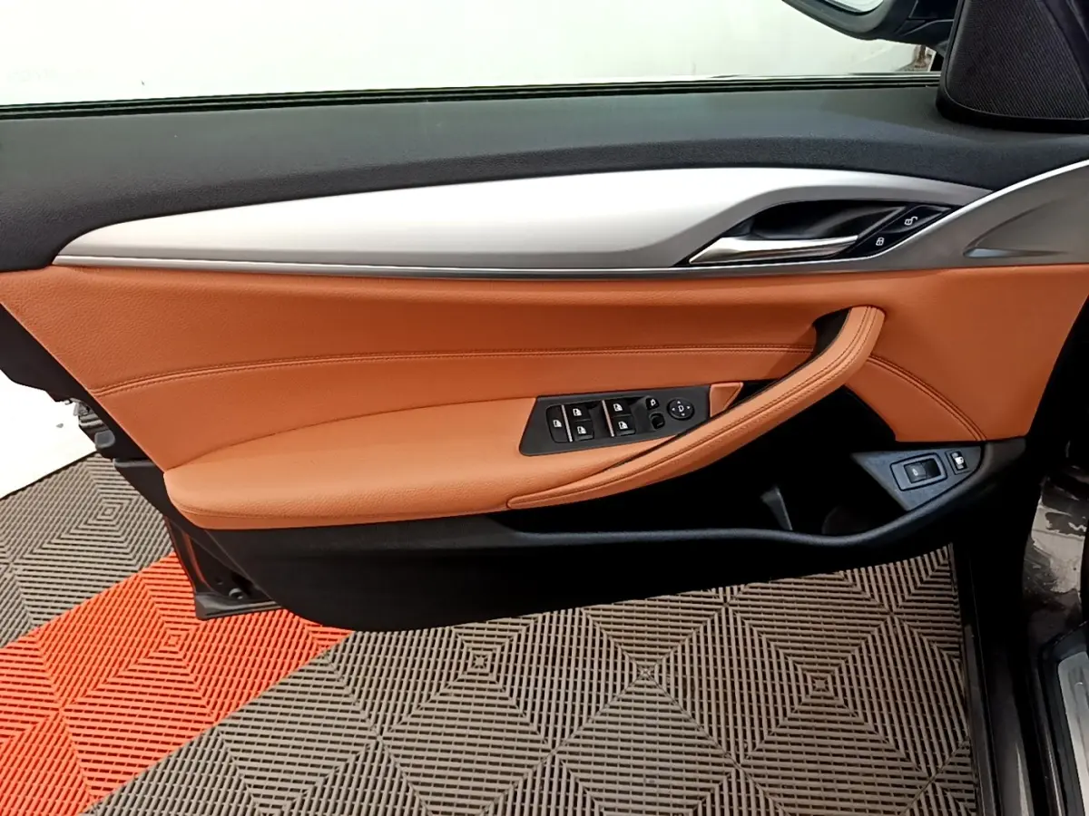 Gros plan sur la porte avant gauche intérieure de la BMW Série 5 Touring 530e avec garniture cuir marron et commandes électriques.
