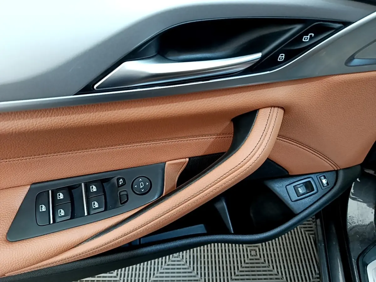 Gros plan sur la porte avant gauche en cuir marron clair avec commandes électriques des vitres et rétroviseurs d'une BMW Série 5 Touring 530e.