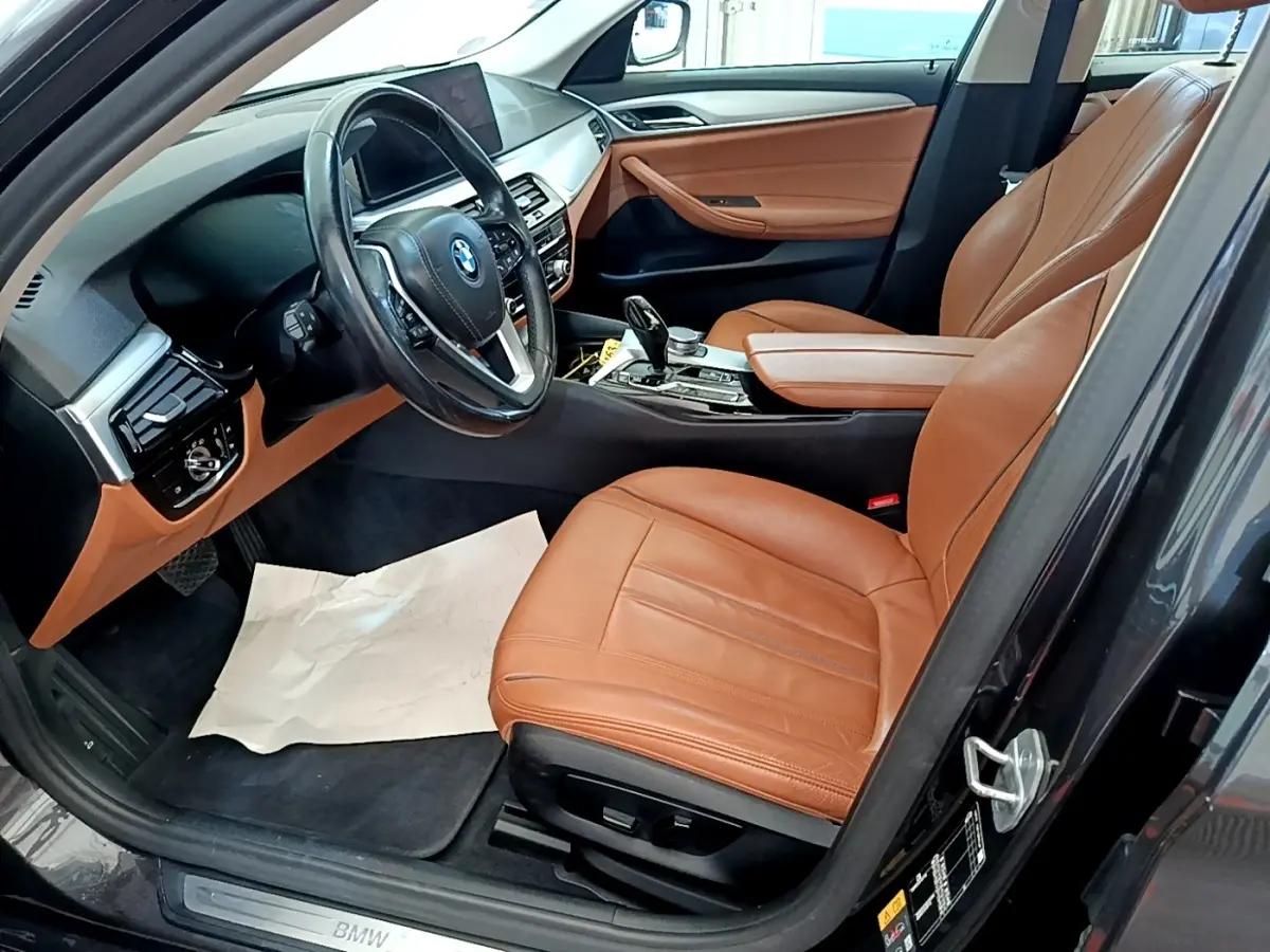 Vue intérieure côté conducteur de la BMW Série 5 Touring 530e 2022 avec sièges cuir marron et tableau de bord gris clair.