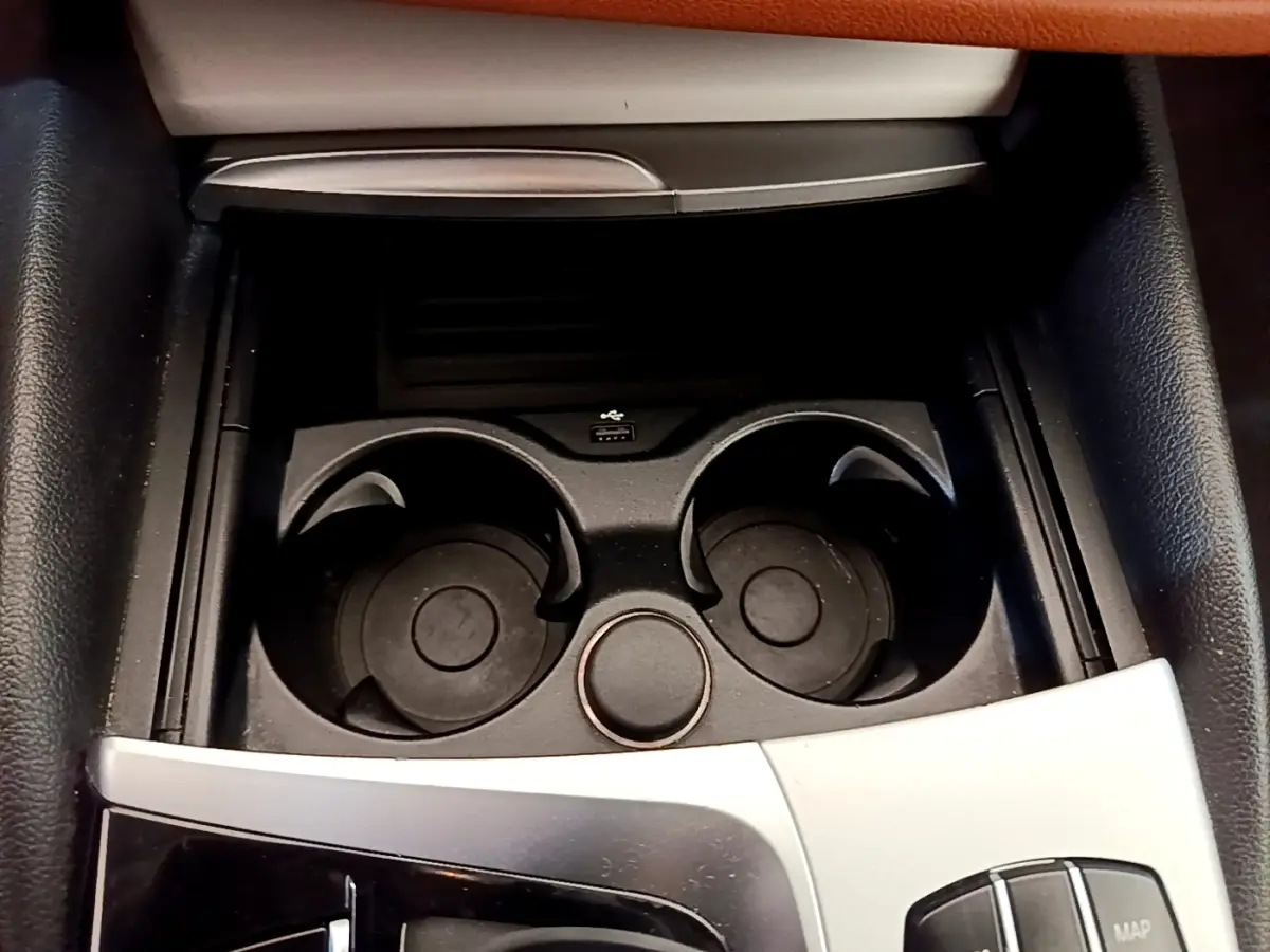 Gros plan sur la console centrale noire avec porte-gobelets et molette de commande dans une BMW Série 5 Touring 530e 2022.