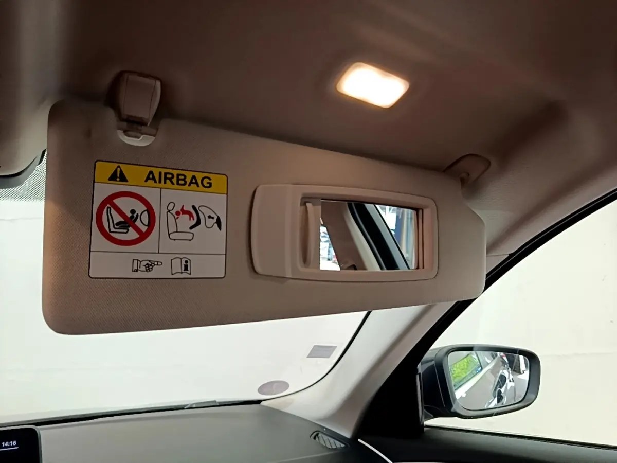 Détail du pare-soleil côté conducteur beige avec miroir intégré et étiquette airbag dans une BMW Série 5 Touring gris clair.