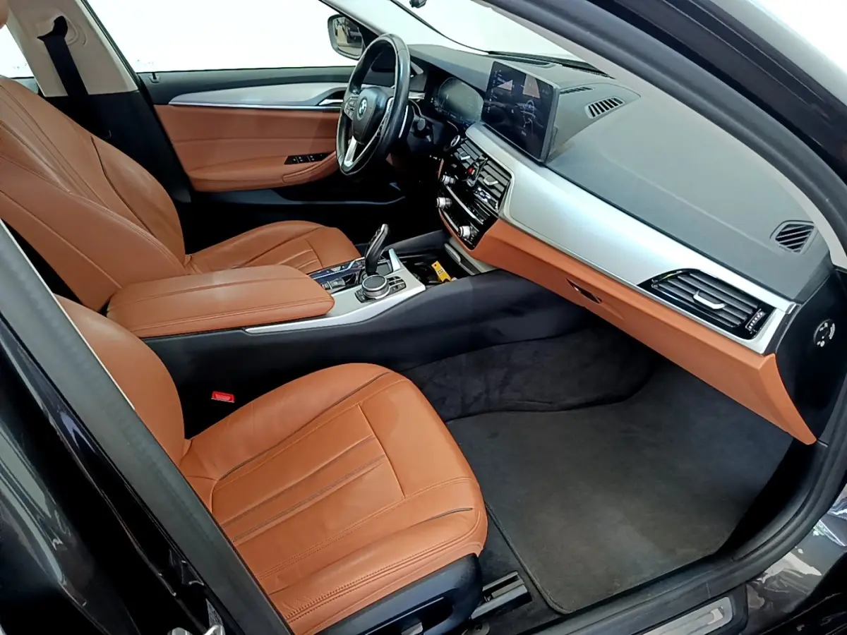 Vue intérieure côté conducteur de la BMW Série 5 Touring 530e 2022 avec sièges cuir marron et tableau de bord moderne.