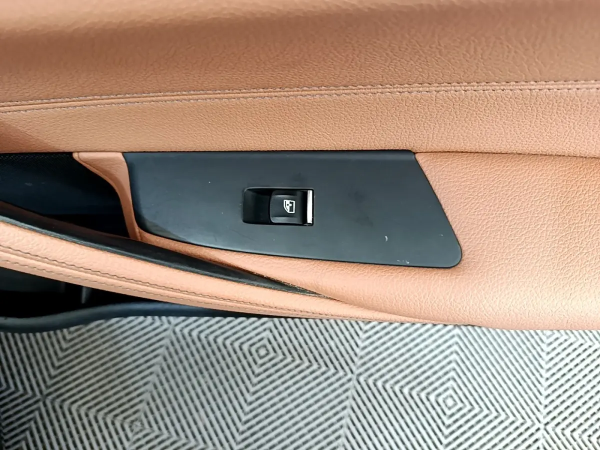 Gros plan sur le bouton de commande de la vitre dans la portière en cuir marron clair d’une BMW Série 5 Touring 530e 2022.