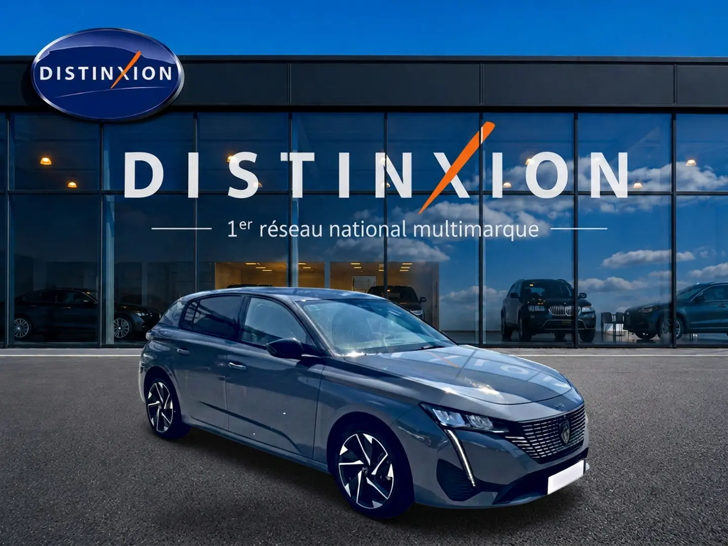 Peugeot 308 gris 3/4 avant droit, jantes alu noires et calandre distinctive, devant vitrine Distinxion.