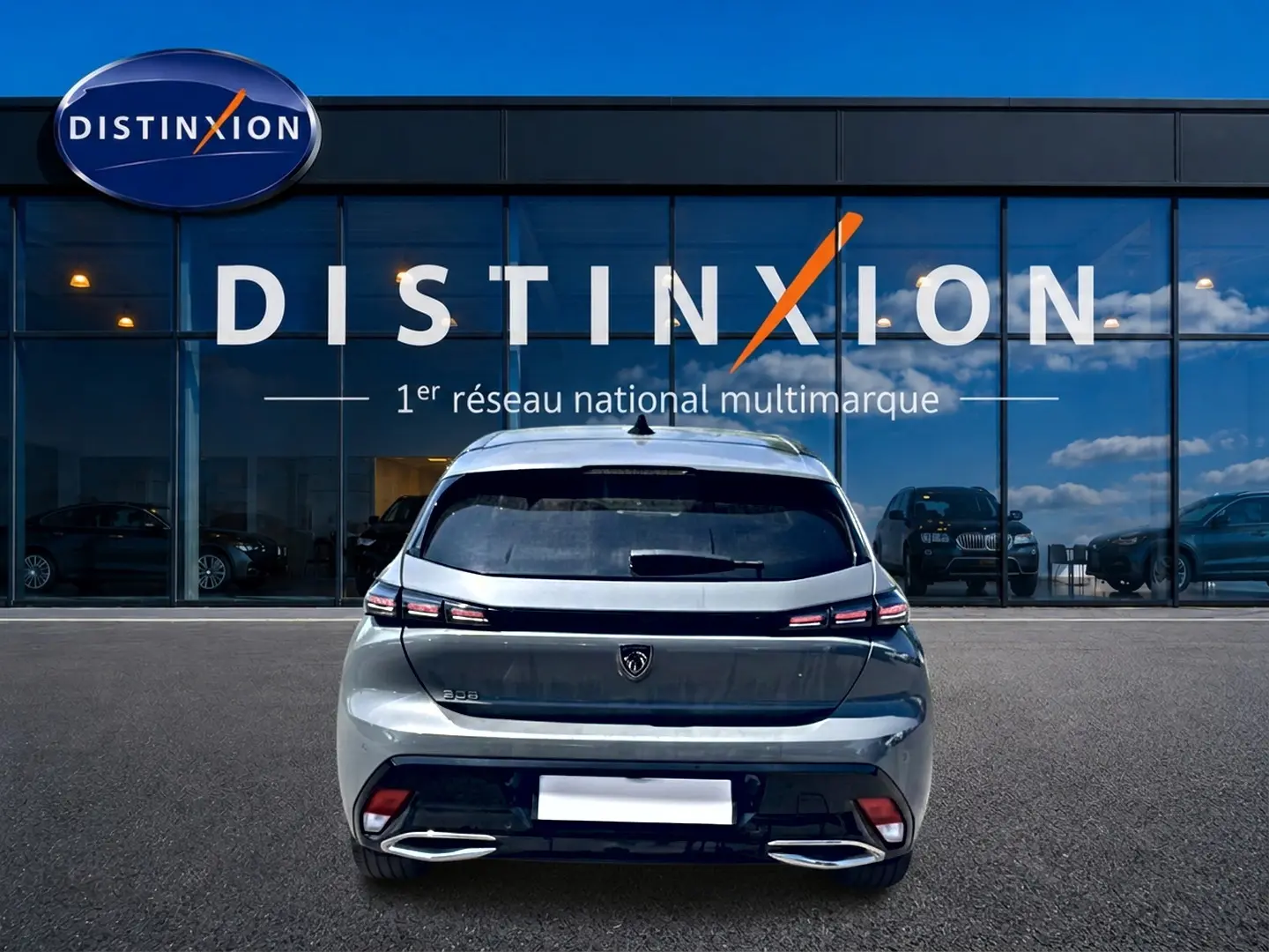 Vue arrière d'une Peugeot 308 gris métallisé 2025 garée devant une vitrine avec logo Distinxion.