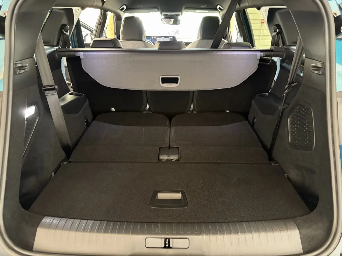 Coffre ouvert en vue arrière d’un Peugeot 5008 vert avec banquette arrière rabattue et cache-bagages déployé.