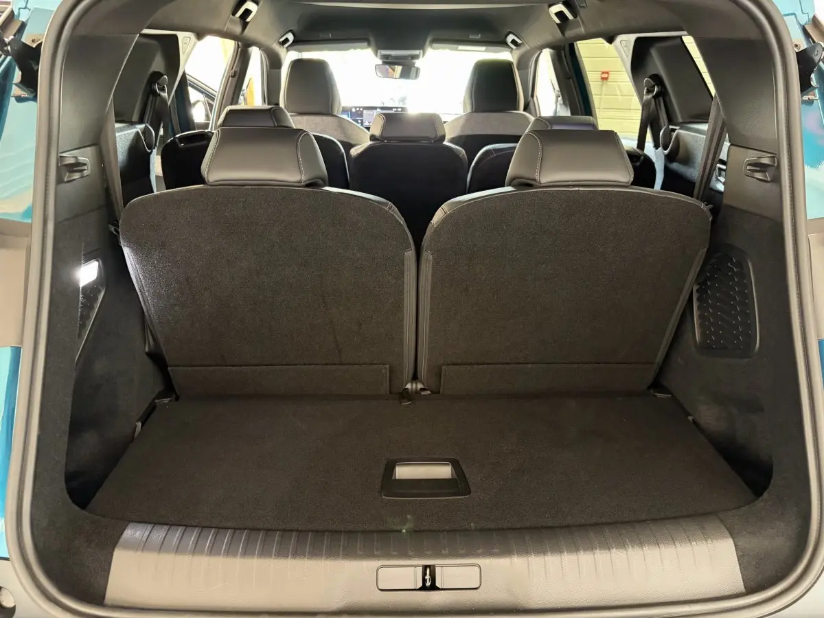 Vue arrière du coffre du Peugeot 5008 hybride vert 2025 avec troisième rangée de sièges rabattus et intérieur noir.