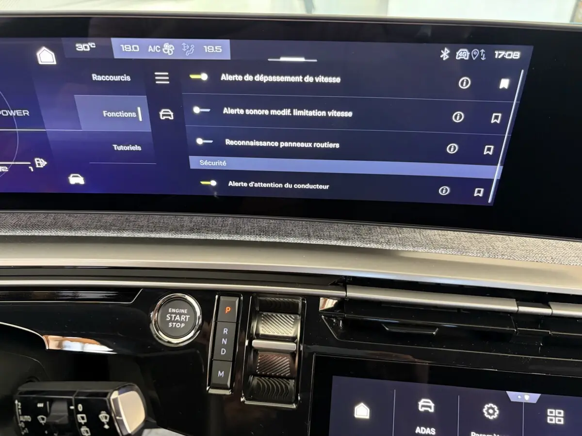 Vue rapprochée du tableau de bord numérique et console centrale du Peugeot 5008 Hybrid vert, avec écran tactile et bouton start/stop.