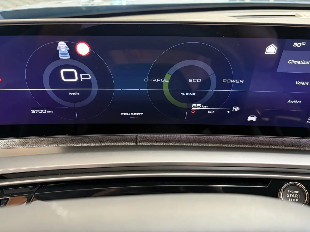 Tableau de bord numérique du Peugeot 5008 hybride, affichage multifonctions avec indicateurs de charge et vitesse, bouton start visible.