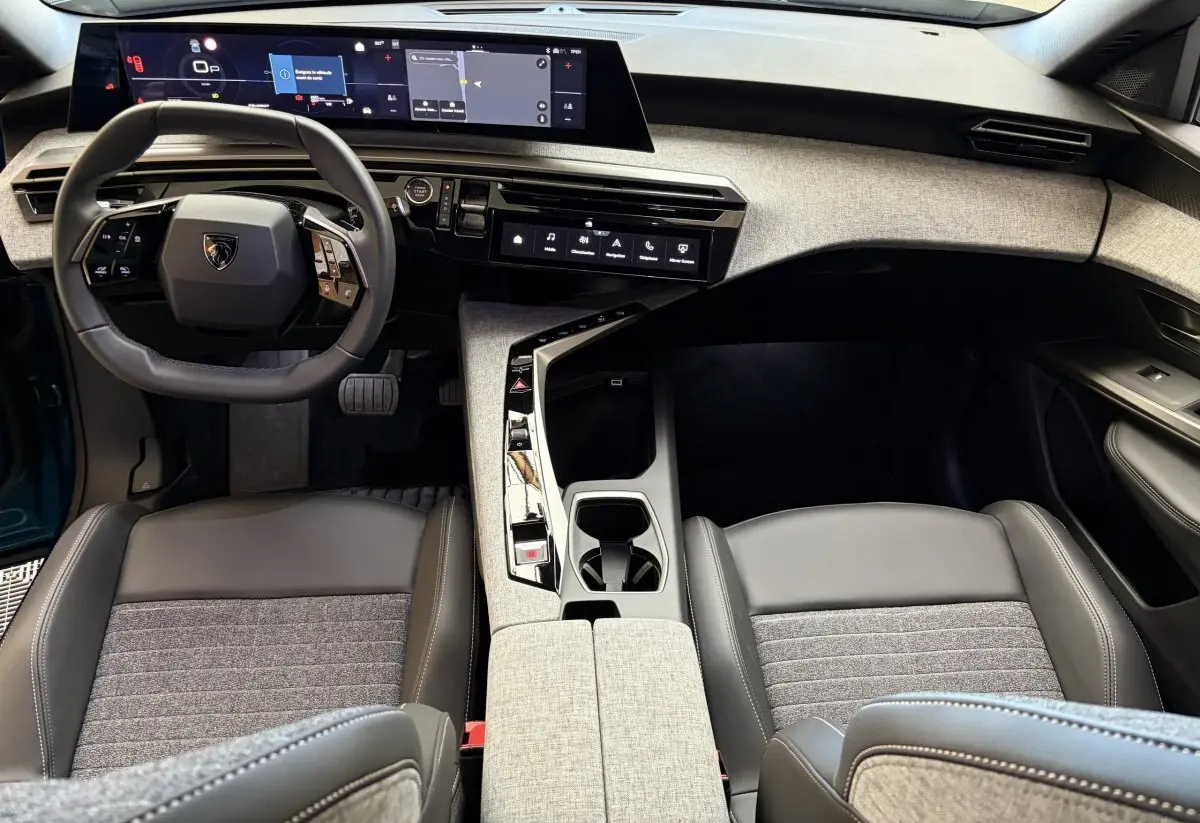 Vue intérieure avant du Peugeot 5008 Hybrid 2025, tableau de bord moderne avec écran large et sièges gris tissu et cuir.