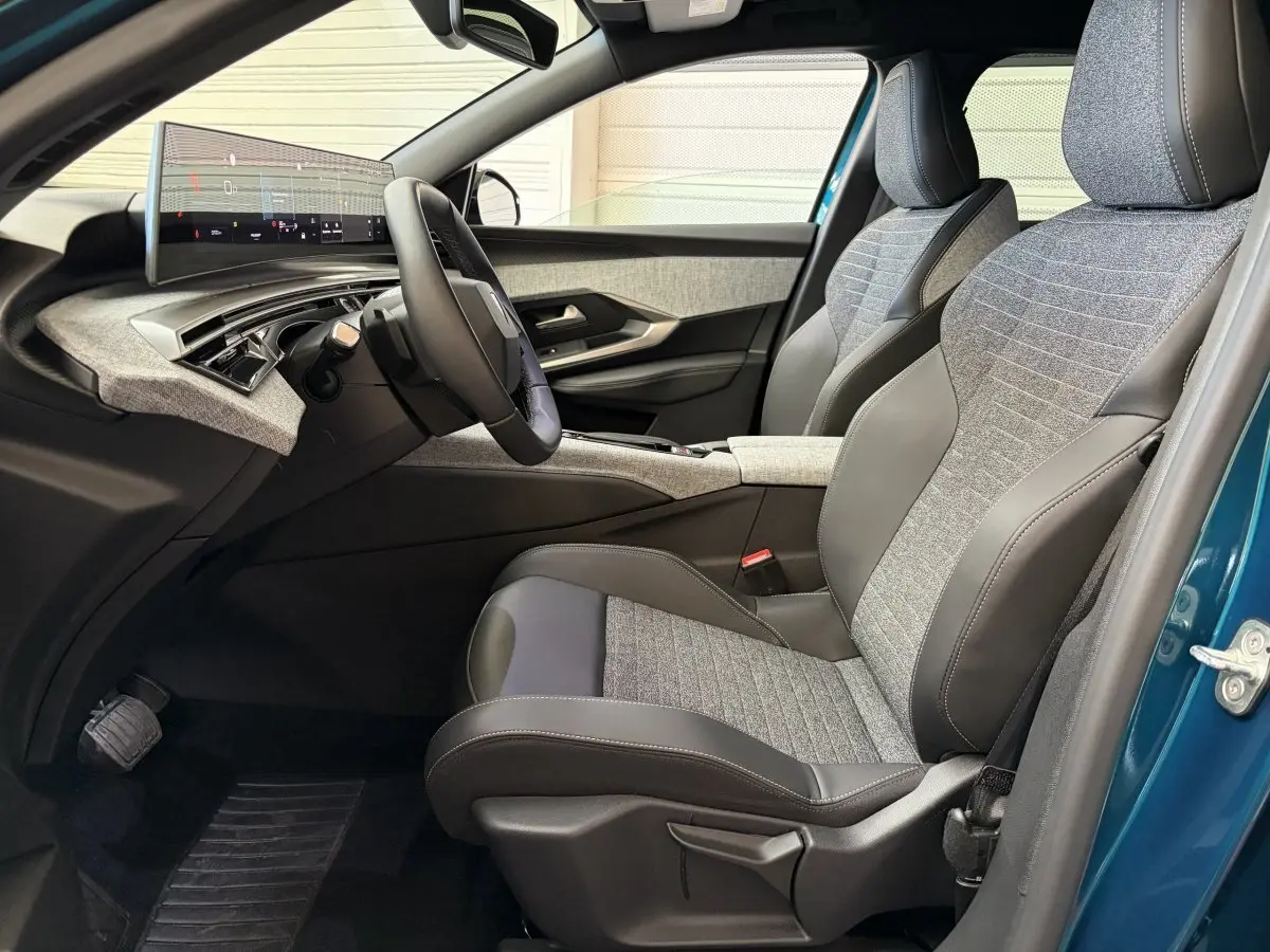 Vue intérieure côté conducteur du Peugeot 5008 Hybrid 145 avec sièges tissu et cuir gris, tableau de bord numérique et portière bleu visible.