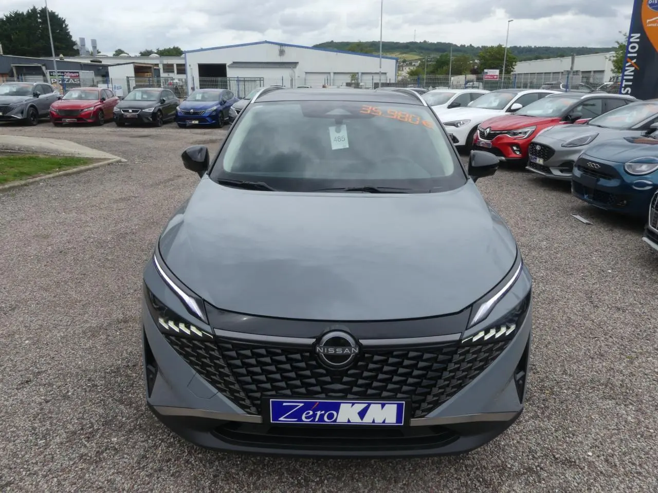 Vue frontale d'un Nissan Qashqai gris métallisé avec calandre noire et feux LED distinctifs sur un parking.