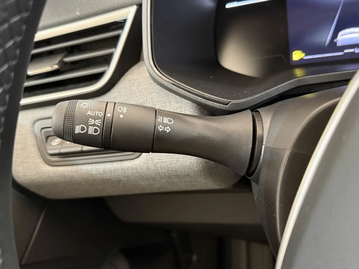 Gros plan sur la commande des phares et clignotants à gauche du volant dans l’habitacle gris clair d’une Renault Clio noire 2025.