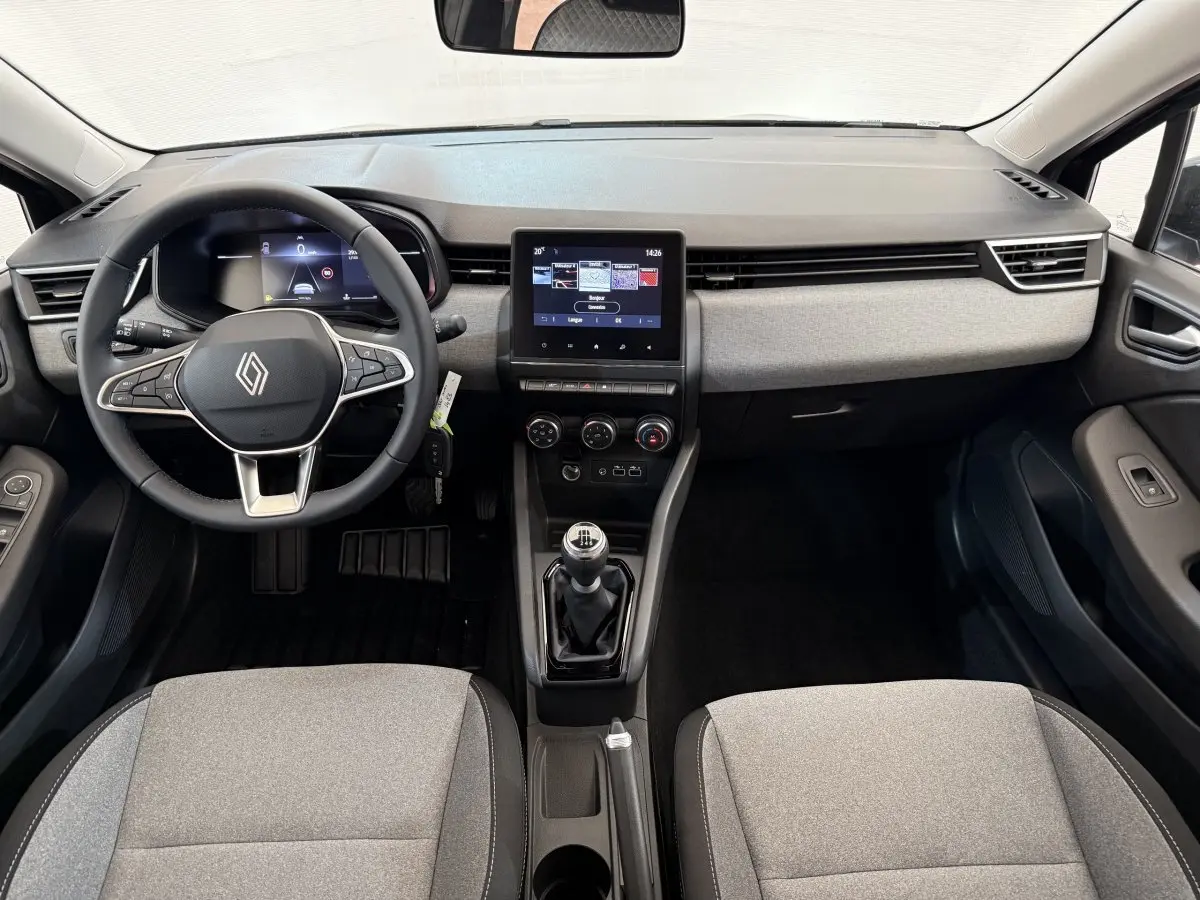 Vue intérieure avant de la Renault Clio 2025 avec tableau de bord gris clair, volant multifonctions et boîte manuelle.