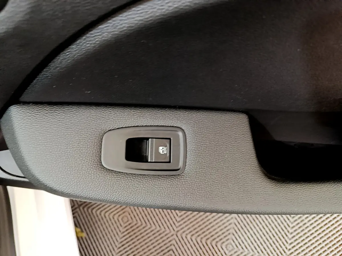 Gros plan sur le bouton de commande de la vitre électrique côté conducteur dans l'habitacle noir d'une Renault Clio blanche 2020.