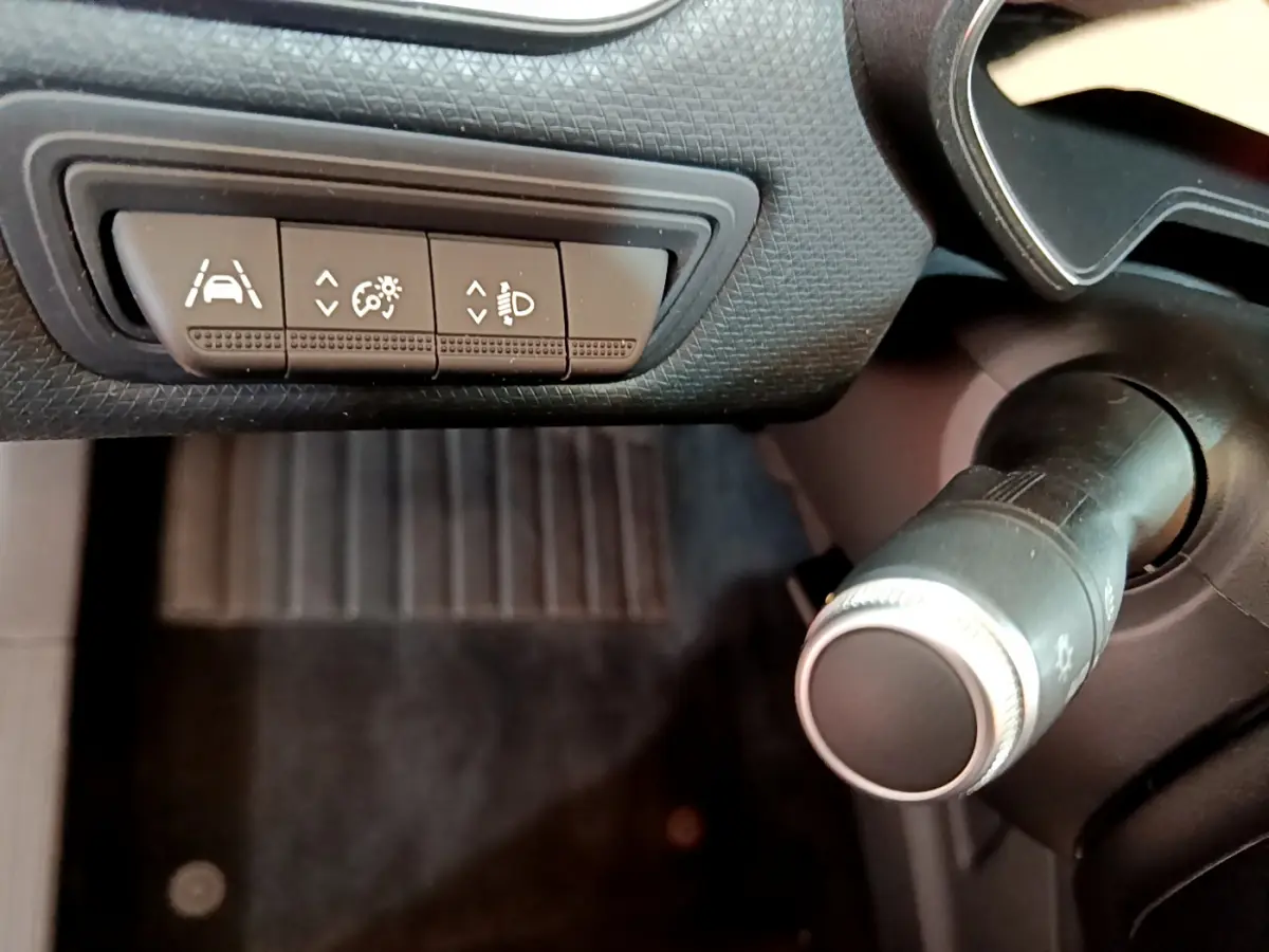 Gros plan sur les commandes d'assistance et réglage des phares côté gauche du tableau de bord noir de la Renault Clio Business blanche.