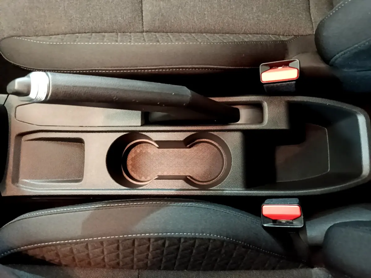 Vue plongeante sur la console centrale noire de la Renault Clio Business avec frein à main manuel et ceintures rouges.