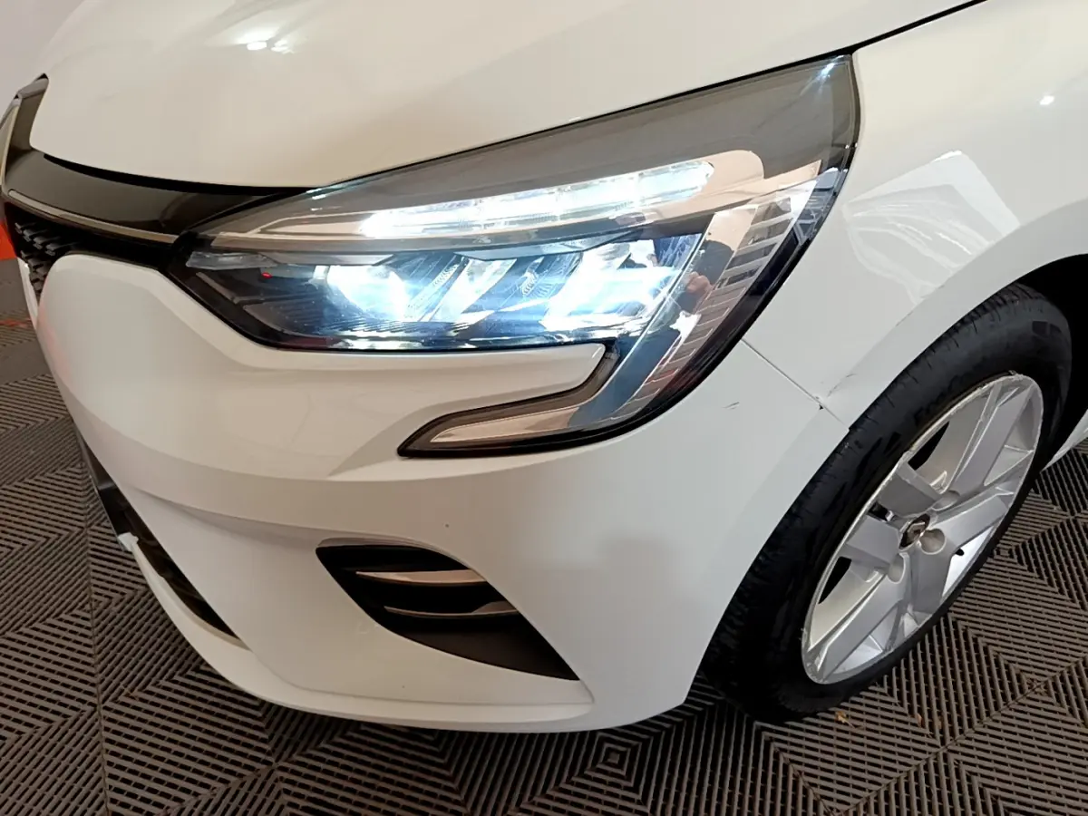 Gros plan sur l'avant droit blanc d'une Renault Clio 2020 avec phares LED allumés et jante alu visible.